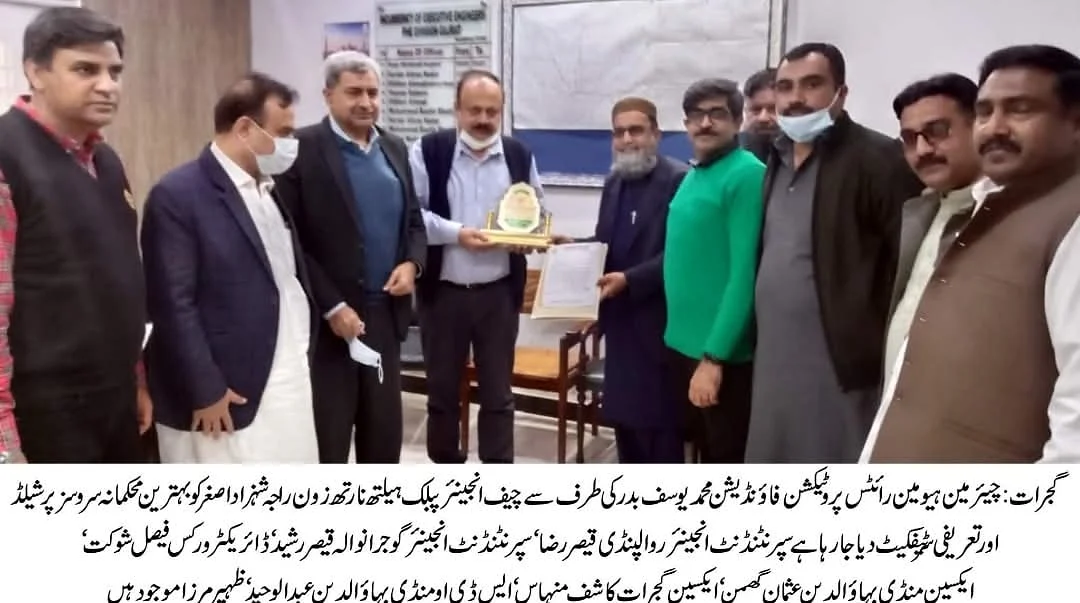 A newspaper photograph of men holding a plaque in an office, with an Urdu caption beneath it.