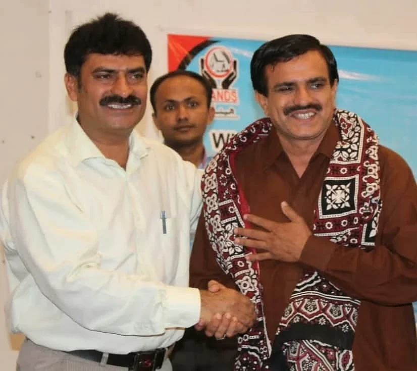 Two men shaking hands, with a third man standing behind them.
