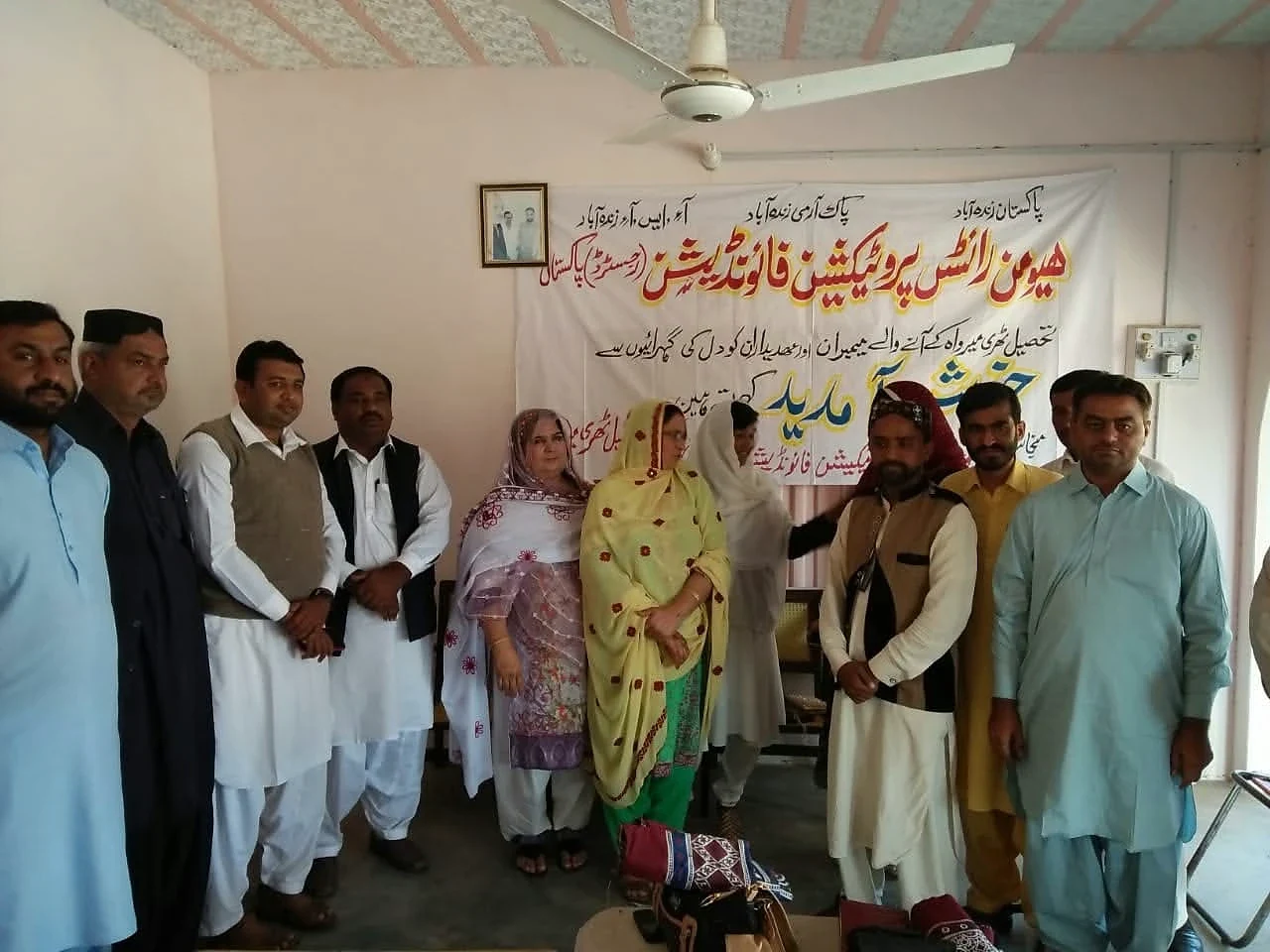 Men and women standing together indoors beneath an Urdu banner.