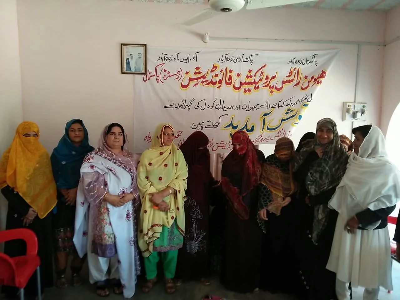 A group of men and women standing beside an Urdu banner in a room.