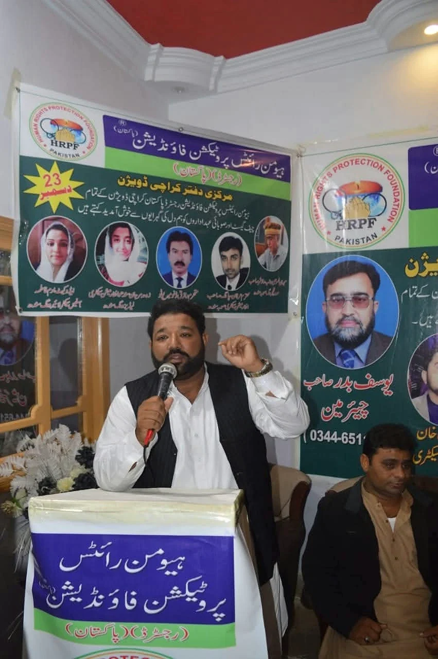A man holding a microphone at an HRPF lectern in front of a portrait banner.