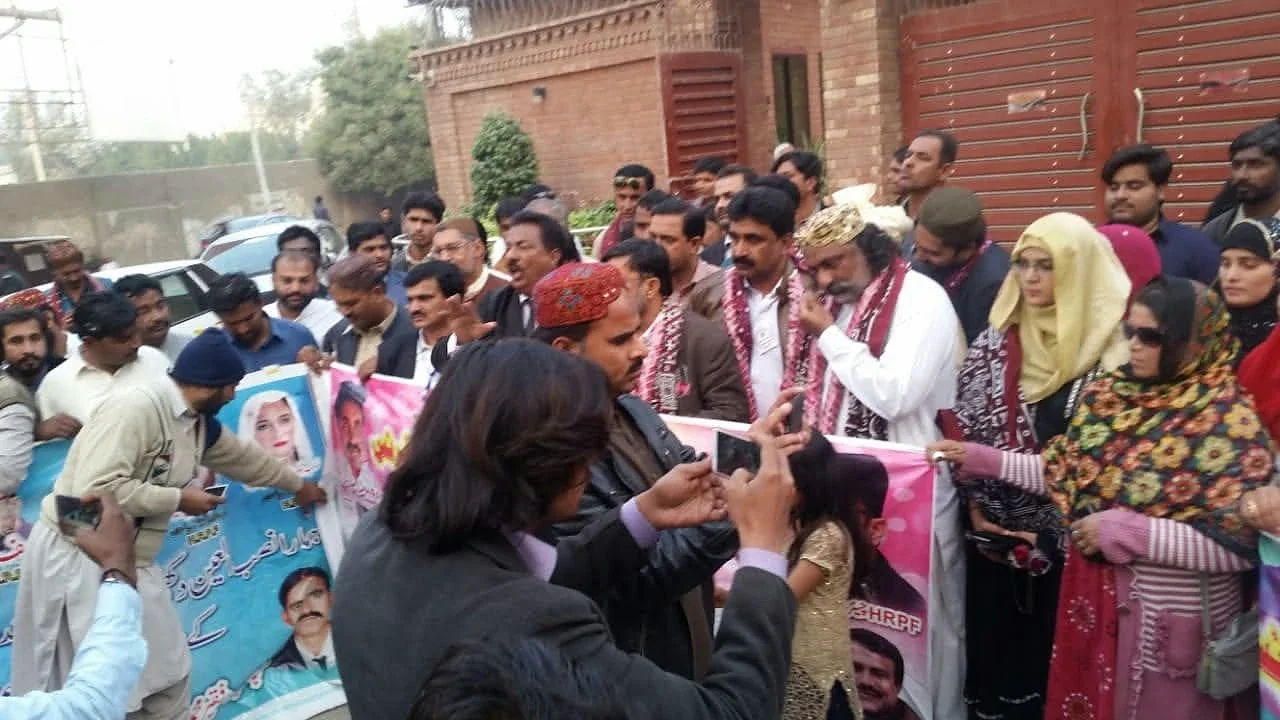 Men and women gathered outside a brick building, with a banner at the front.