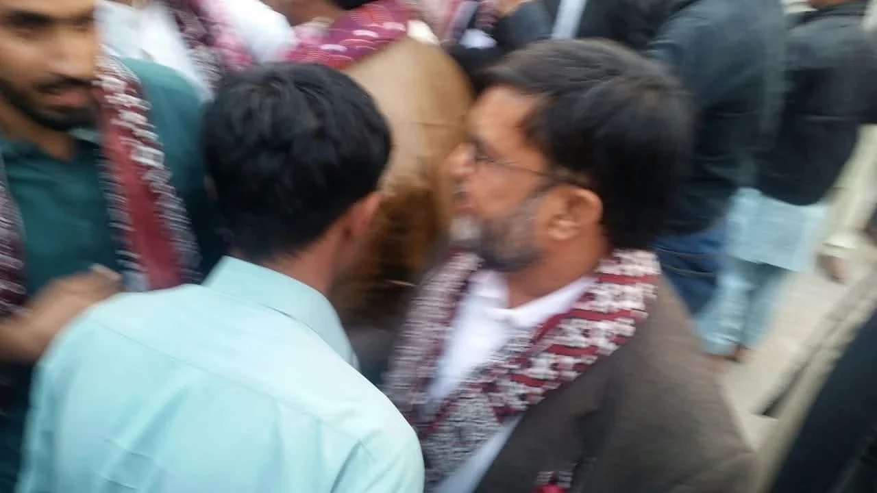 Two men greeting each other amid a crowd at an outdoor gathering.