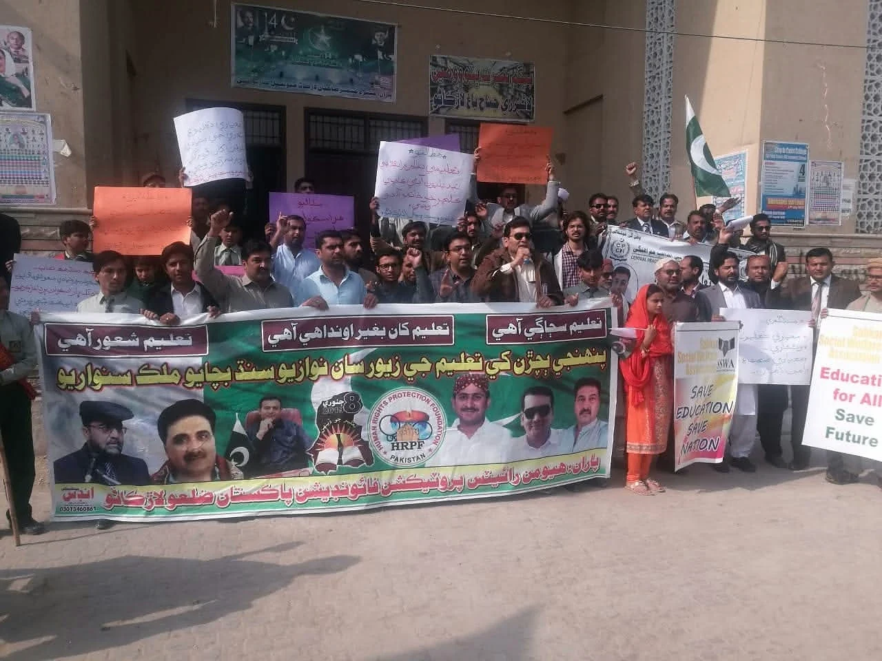 People holding a large printed banner and coloured placards outside a building.