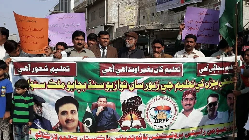 A group holding a printed banner with portraits, with placards raised behind them.