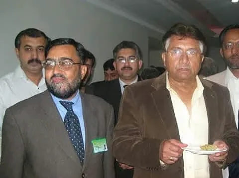 Two men standing in front of other attendees at an indoor gathering.