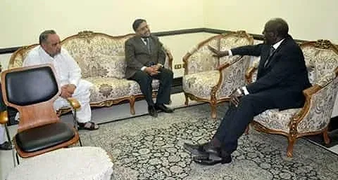 Three men seated on upholstered furniture in a formal room.