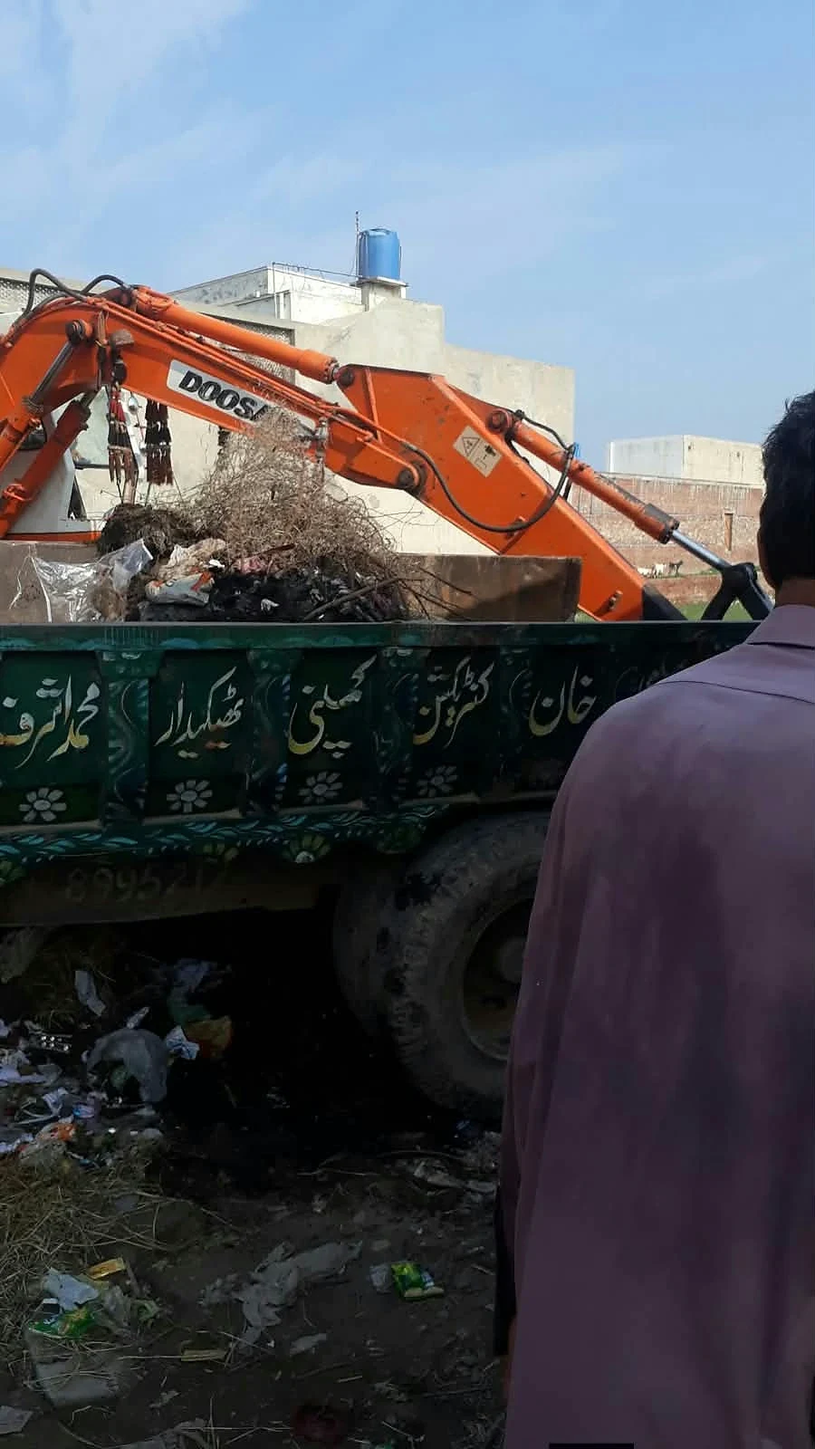 An orange excavator beside a channel containing accumulated waste.