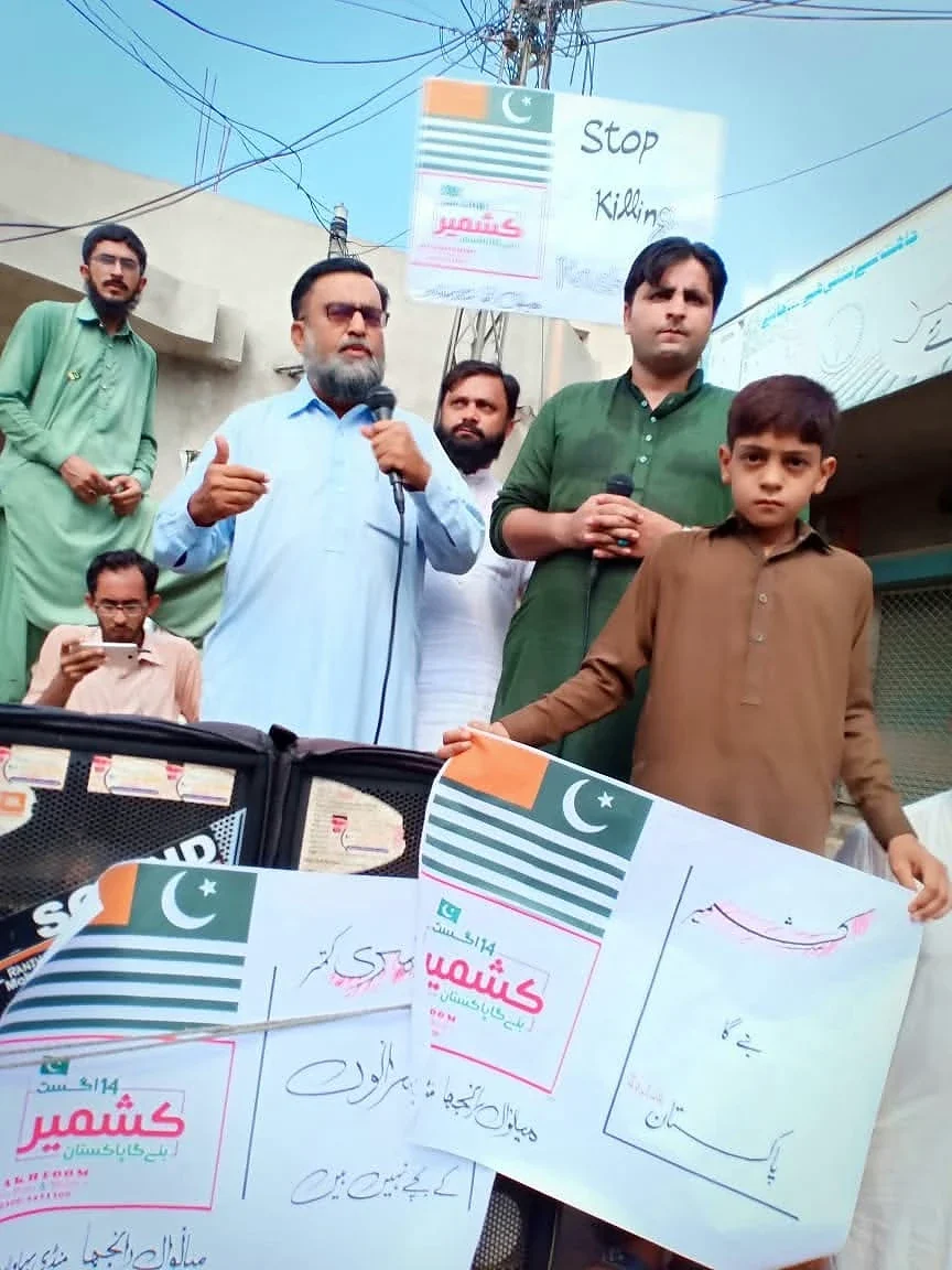 Adults and a child standing in a street holding placards with Pakistan flags and Kashmir text.