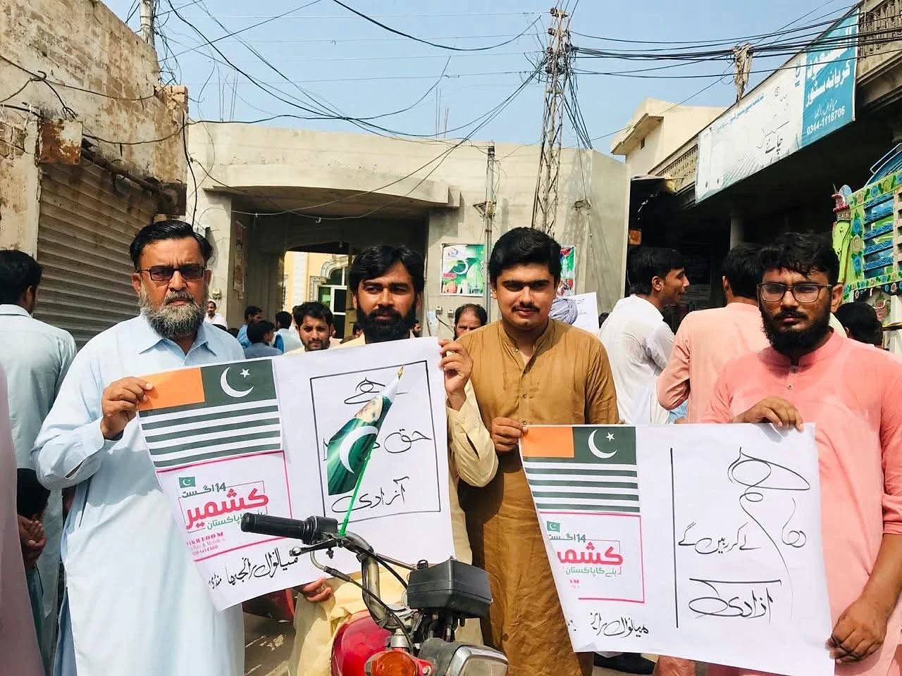 Men standing in a street with placards bearing Pakistan flags and Kashmir text.