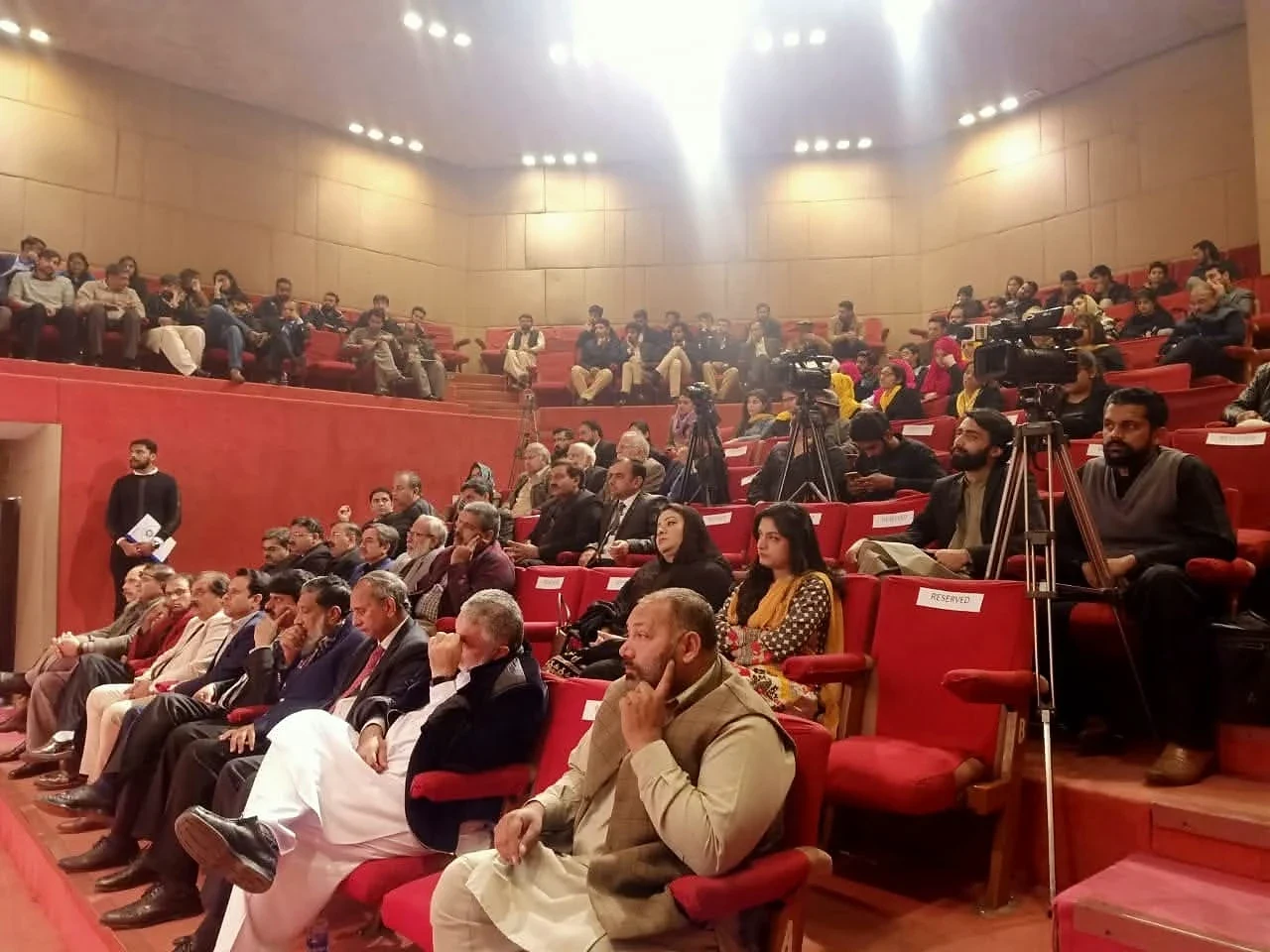 People seated in red chairs facing the front of an auditorium.