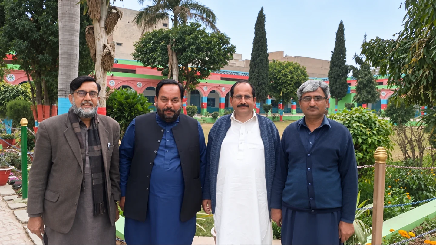 Four men standing together beside flowers and trees in a garden.