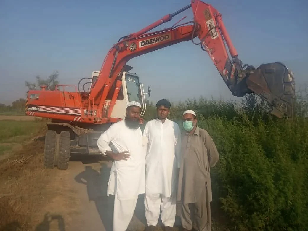 Three men standing in front of an orange excavator outdoors.