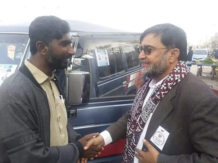 Two men shaking hands outdoors beside parked vehicles.