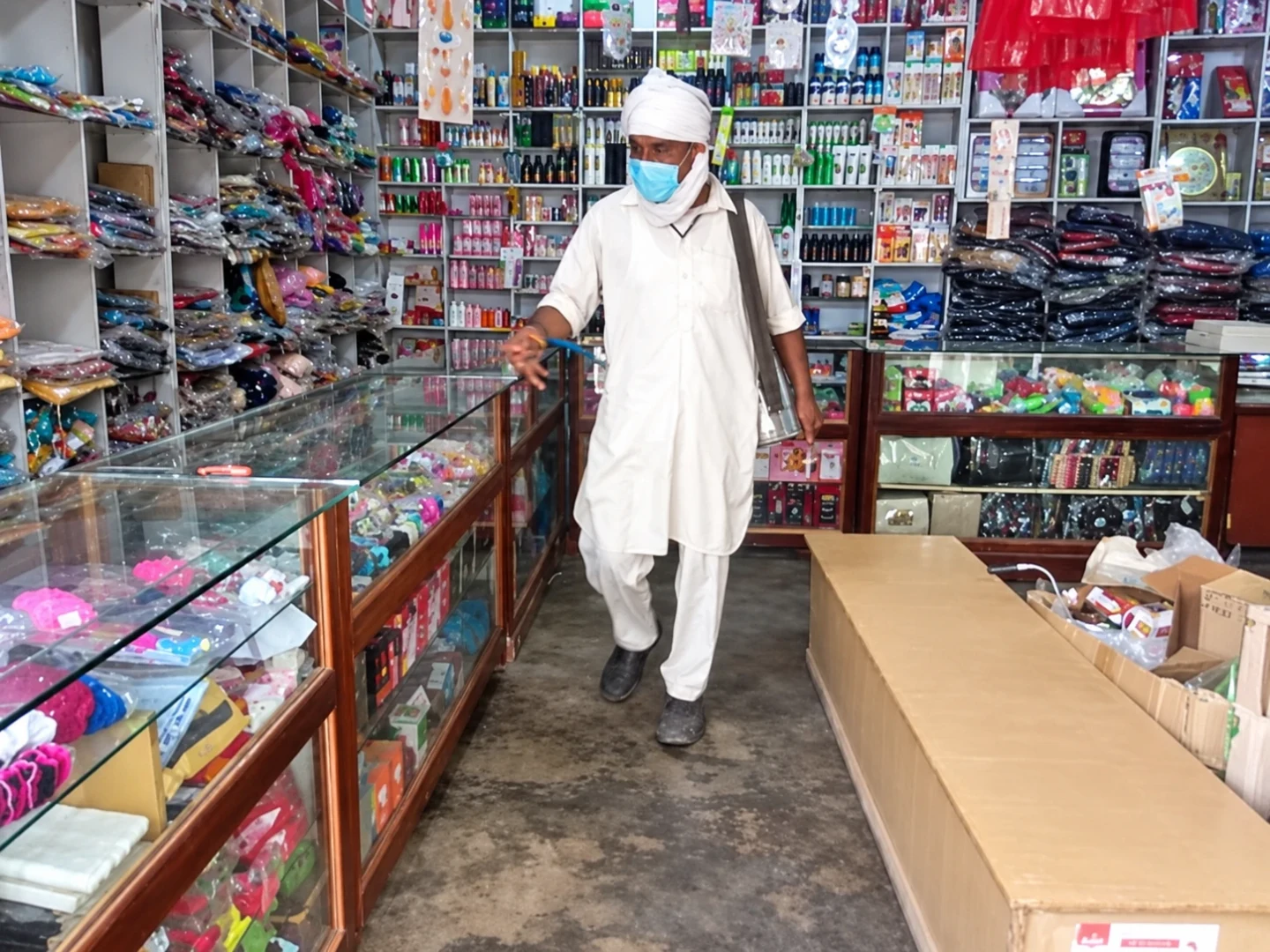 A masked person in white clothing standing between stocked shop shelves.