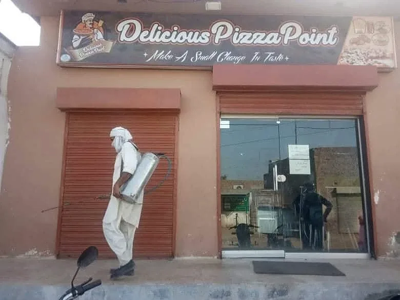 A person in white clothing carrying a container outside a pizza shop.