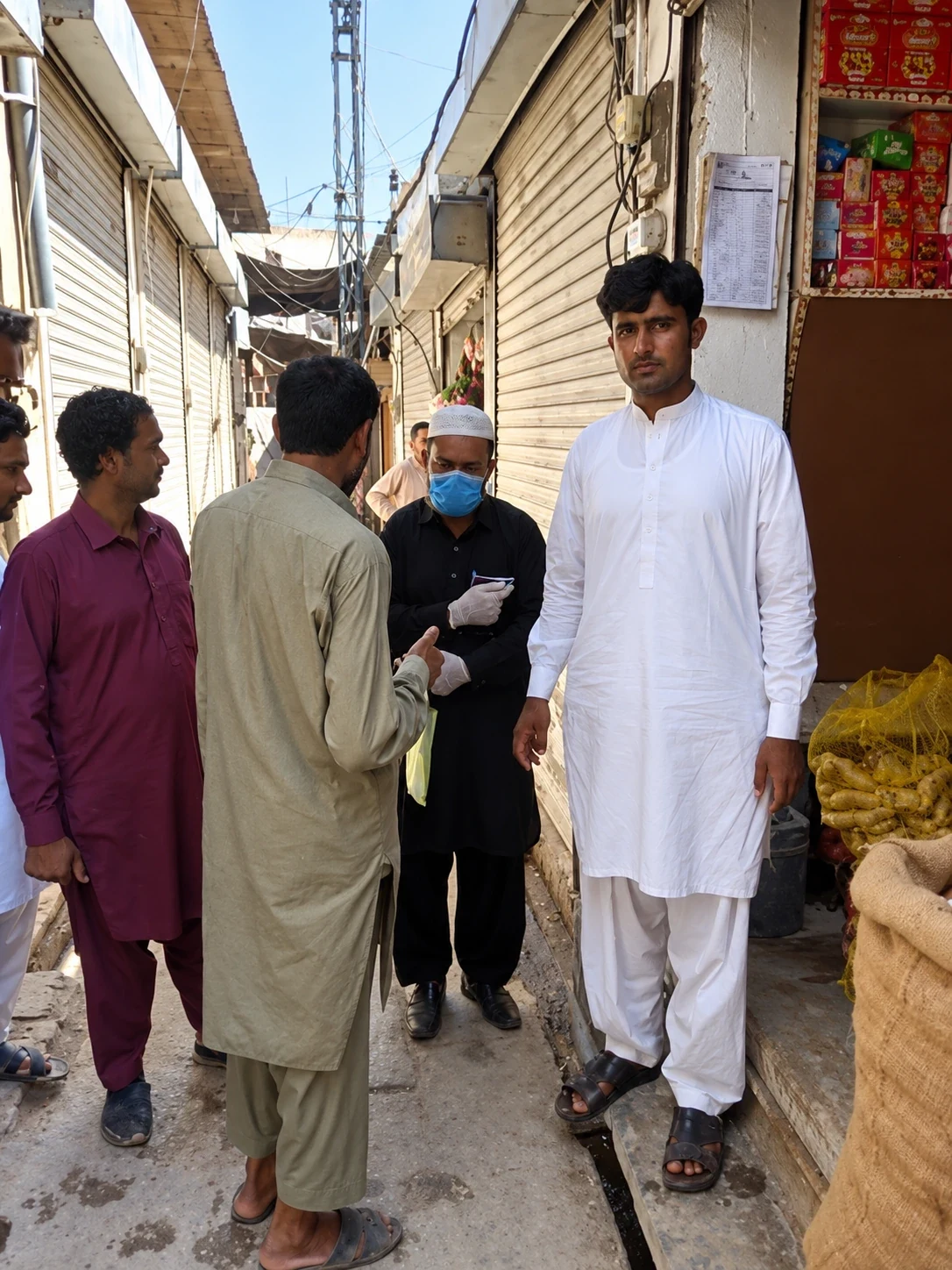 People standing in a narrow shopping lane beside shuttered and open shops.
