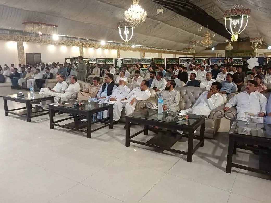 People seated on sofas and chairs facing the front of a decorated hall.