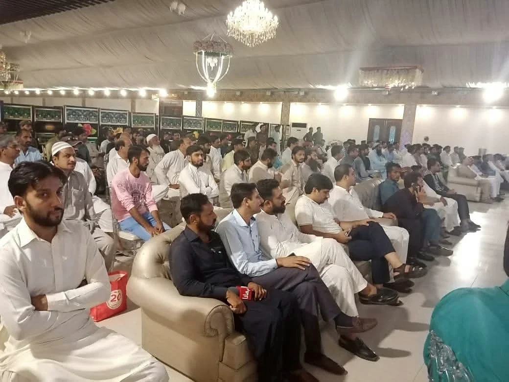 Men seated in the front row of a large indoor meeting hall.