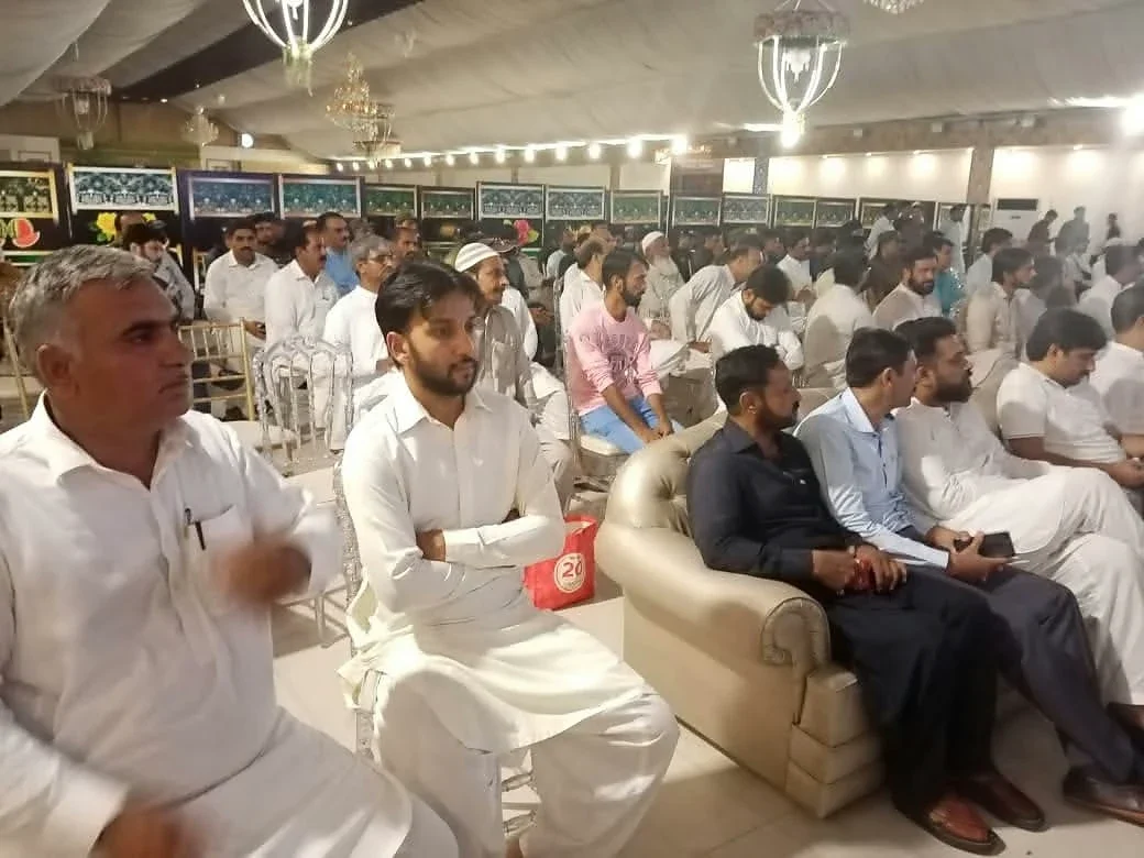Men seated on sofas in the front row of a decorated meeting hall.