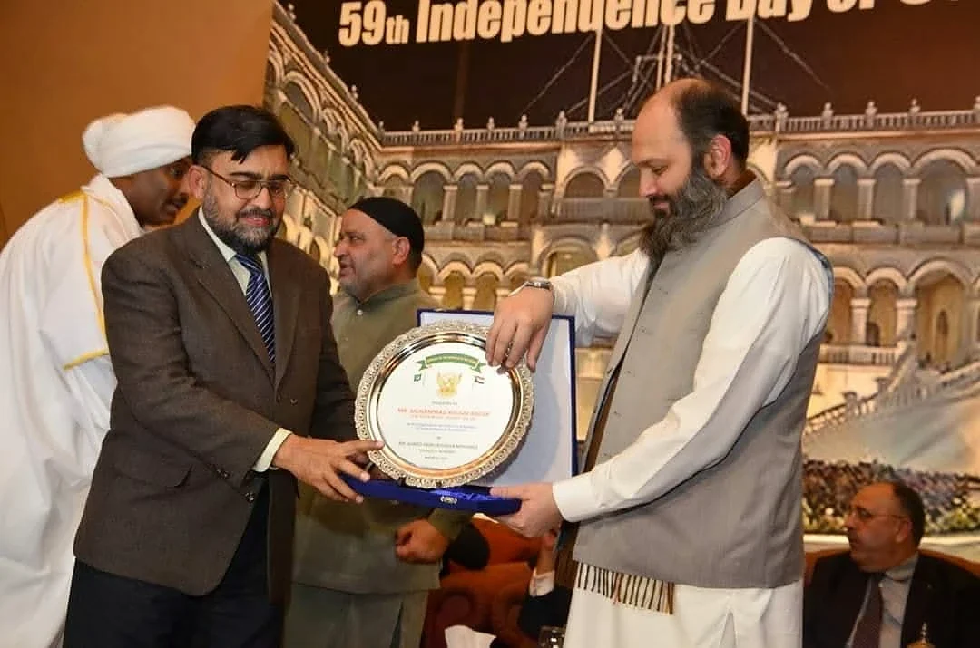 Two men holding a round presentation plaque at a formal reception.