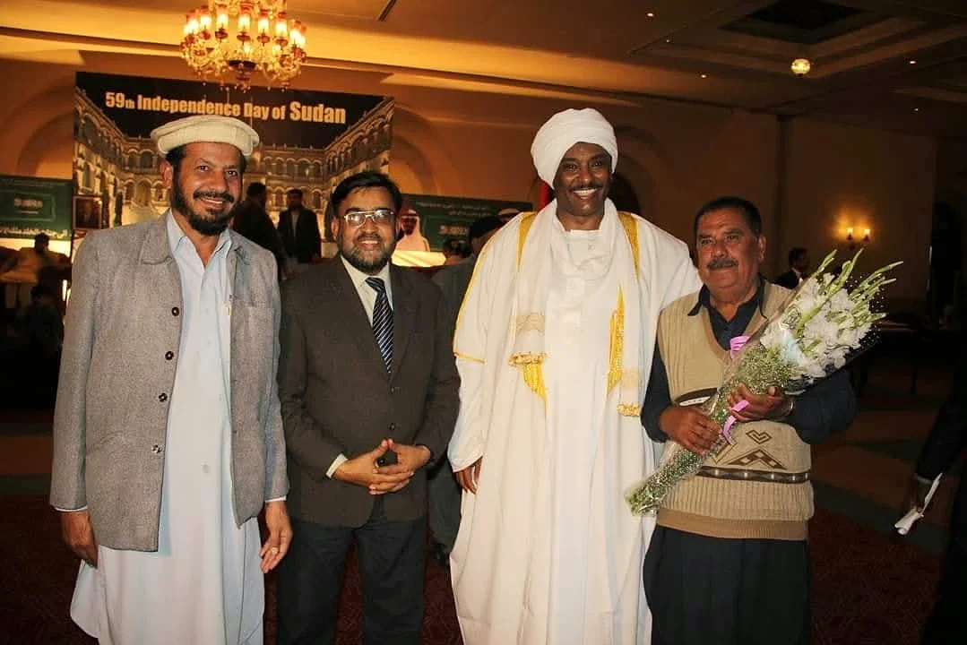 Four men posing together at a reception, with one holding a bouquet.