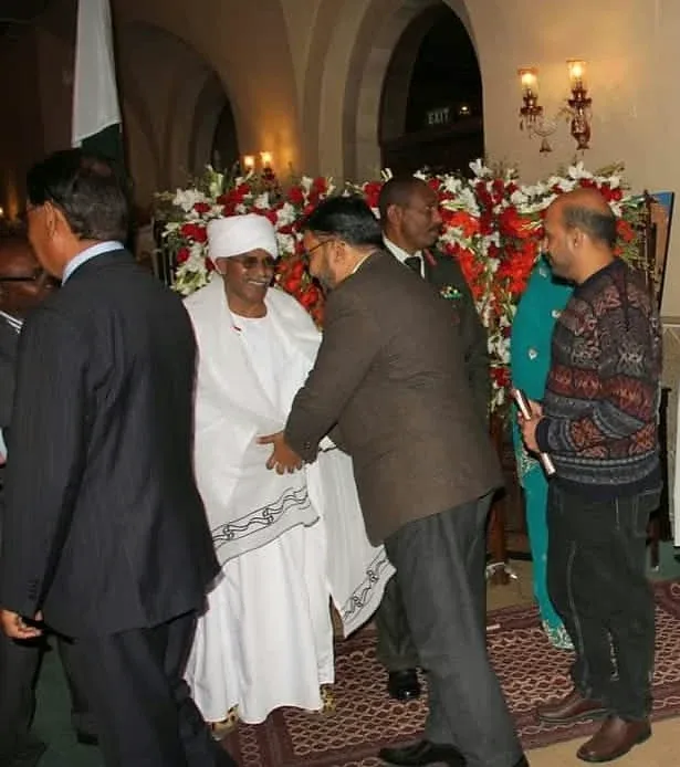 A group of guests standing beside floral arrangements at an indoor reception.