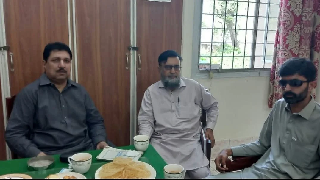 Three men seated around a table with cups and plates in a room.