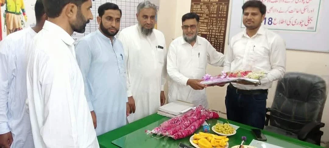Men standing around a green table, with two holding a tray of flowers.
