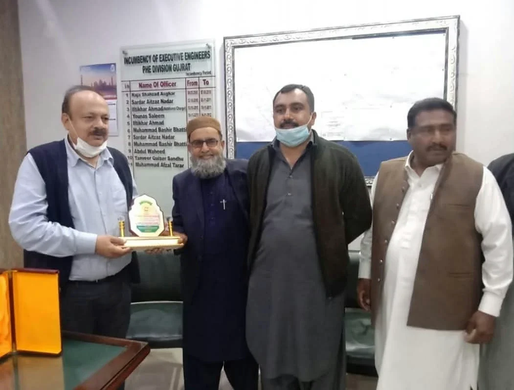 Four men posing in an office, with one holding a small presentation plaque.