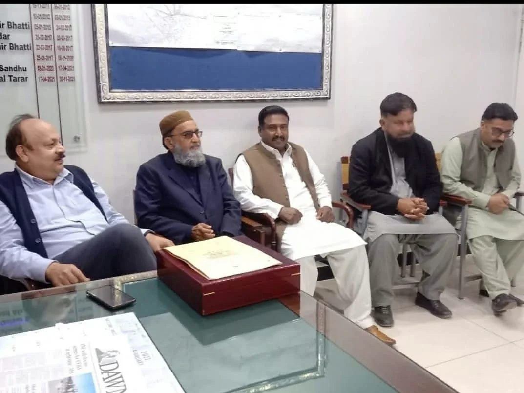 Five men seated beside an office desk with papers and a presentation case.