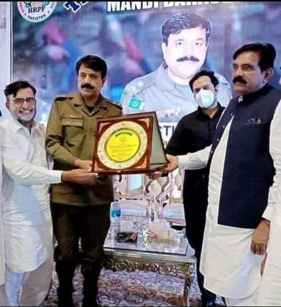A uniformed man and other participants holding a presentation plaque on a stage.