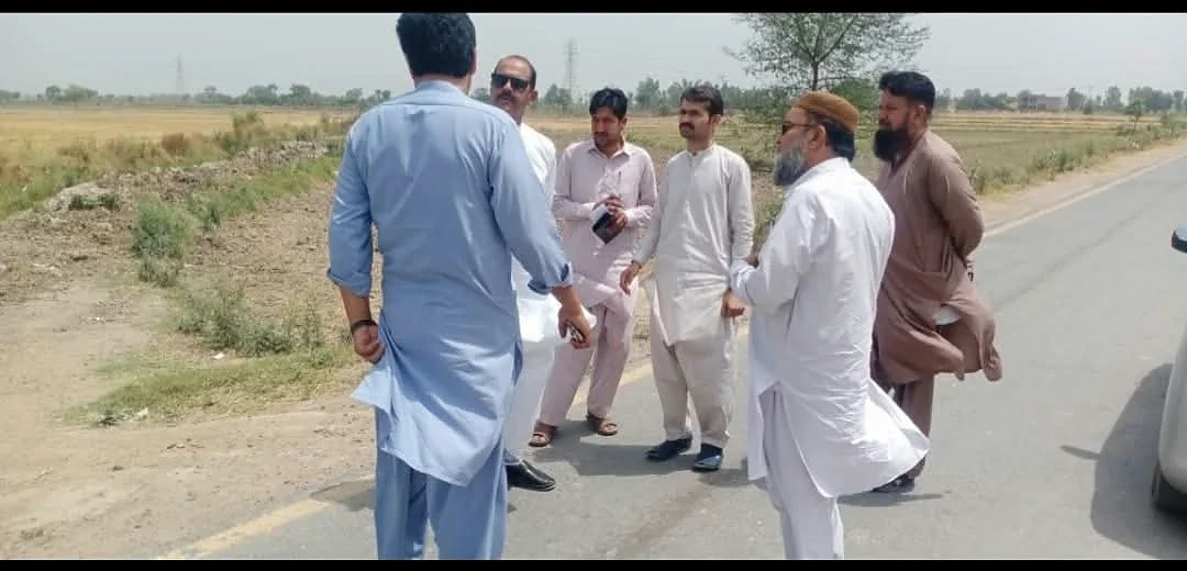 Men standing beside a rural road and fields during a discussion.