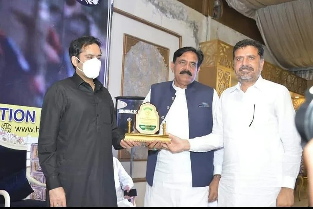 Three men posing in front of an event backdrop with a small presentation plaque.