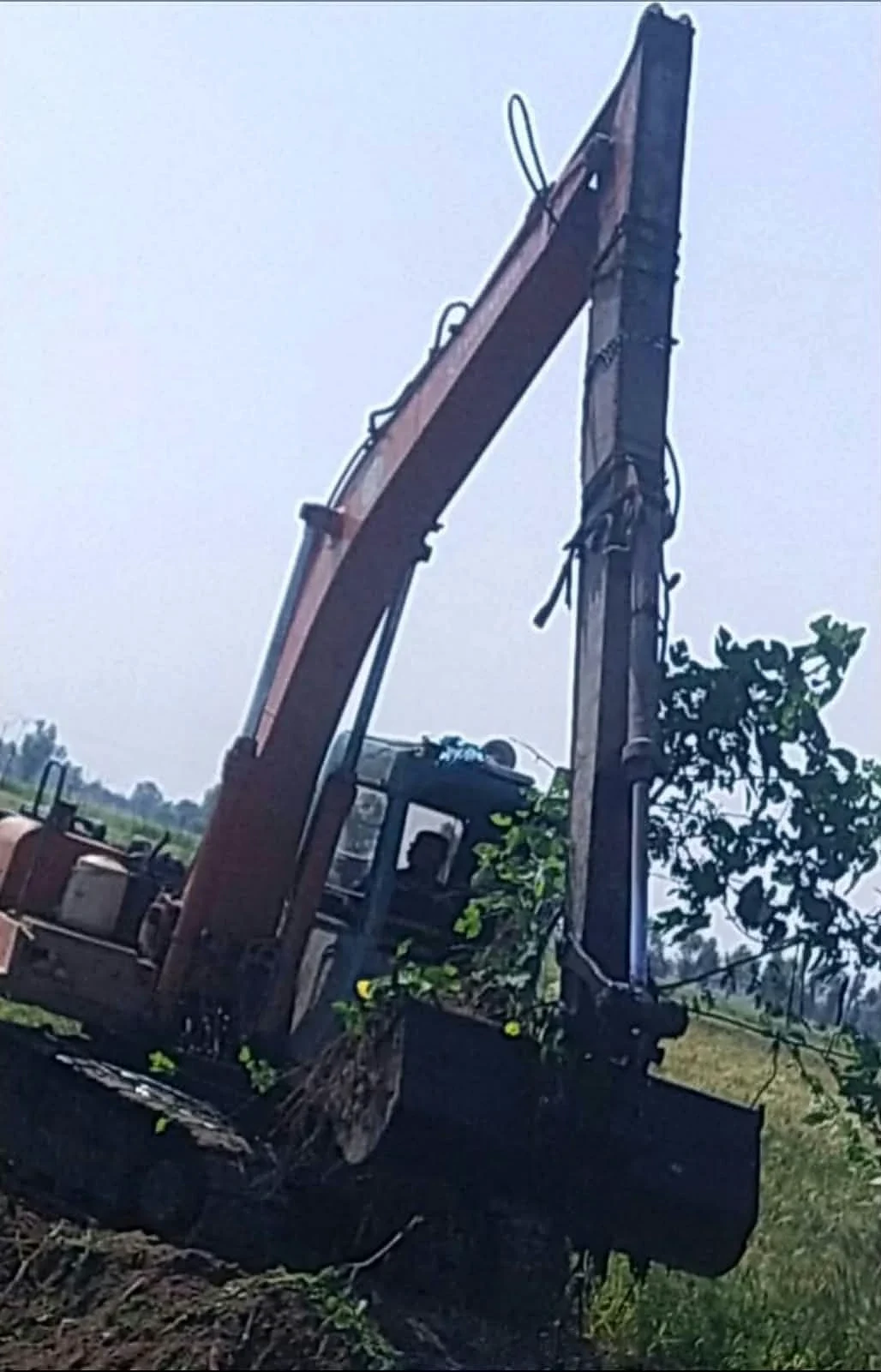 An excavator with its bucket near a channel beside green fields.
