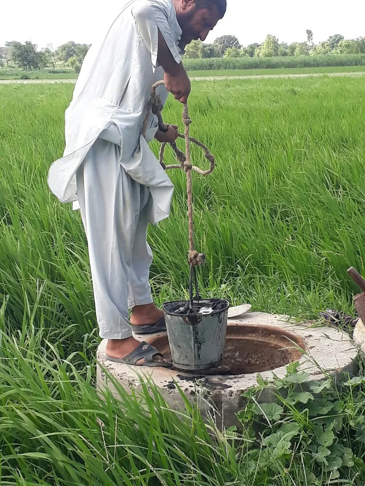 A man holding a rope beside a circular opening in a green field.