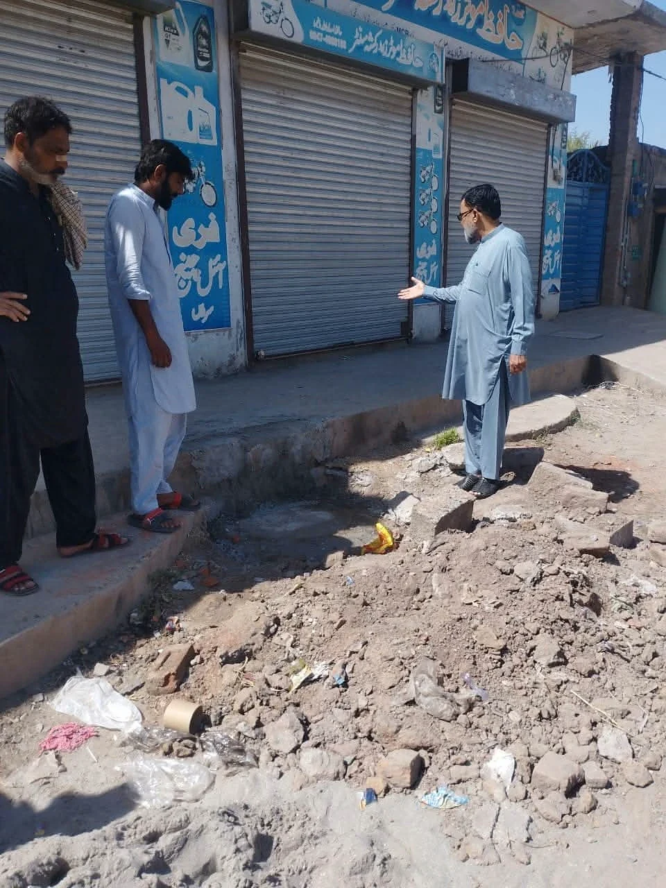 People standing beside an excavated strip of ground outside shuttered shops.