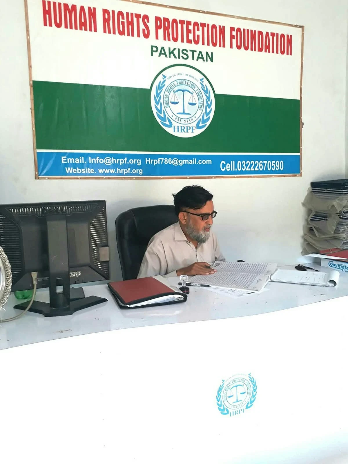 A man seated at a desk beneath a Human Rights Protection Foundation Pakistan sign.