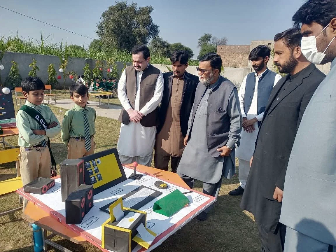 Children beside a display table with adult visitors looking at school projects.