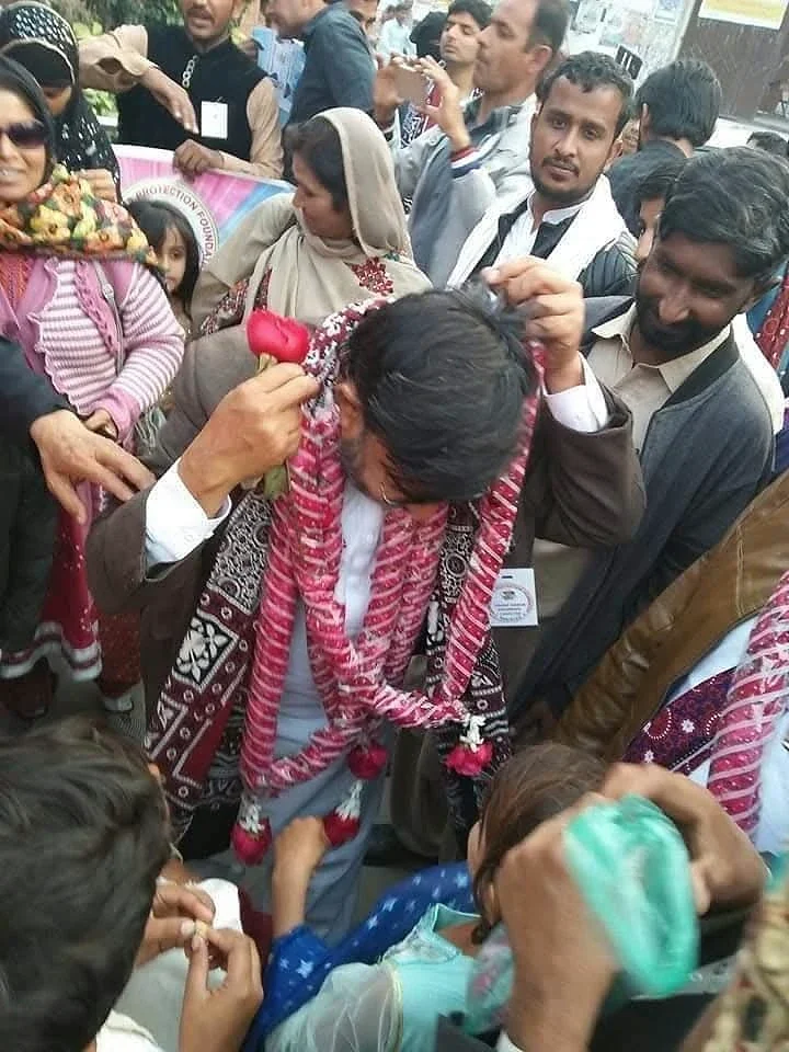 People gathered closely around a man wearing flower garlands and a patterned shawl.