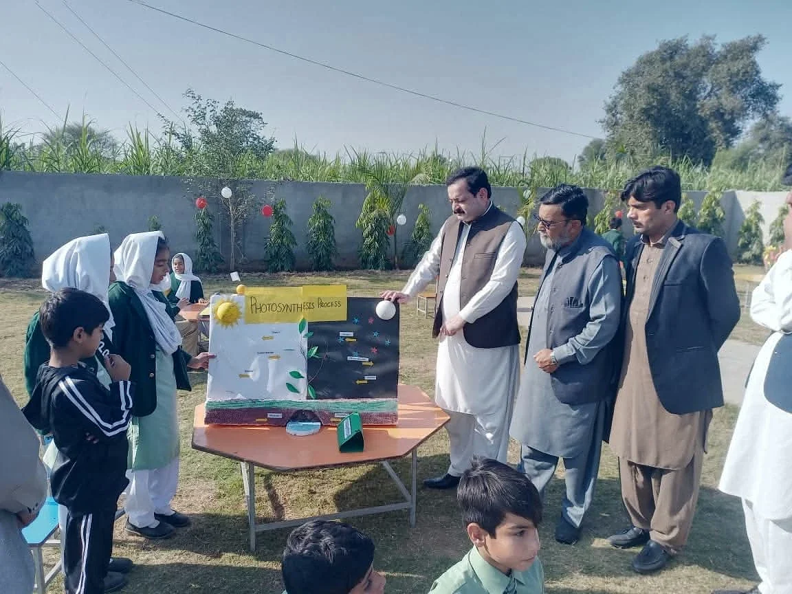 Children presenting colourful displays to adult visitors in an outdoor school setting.
