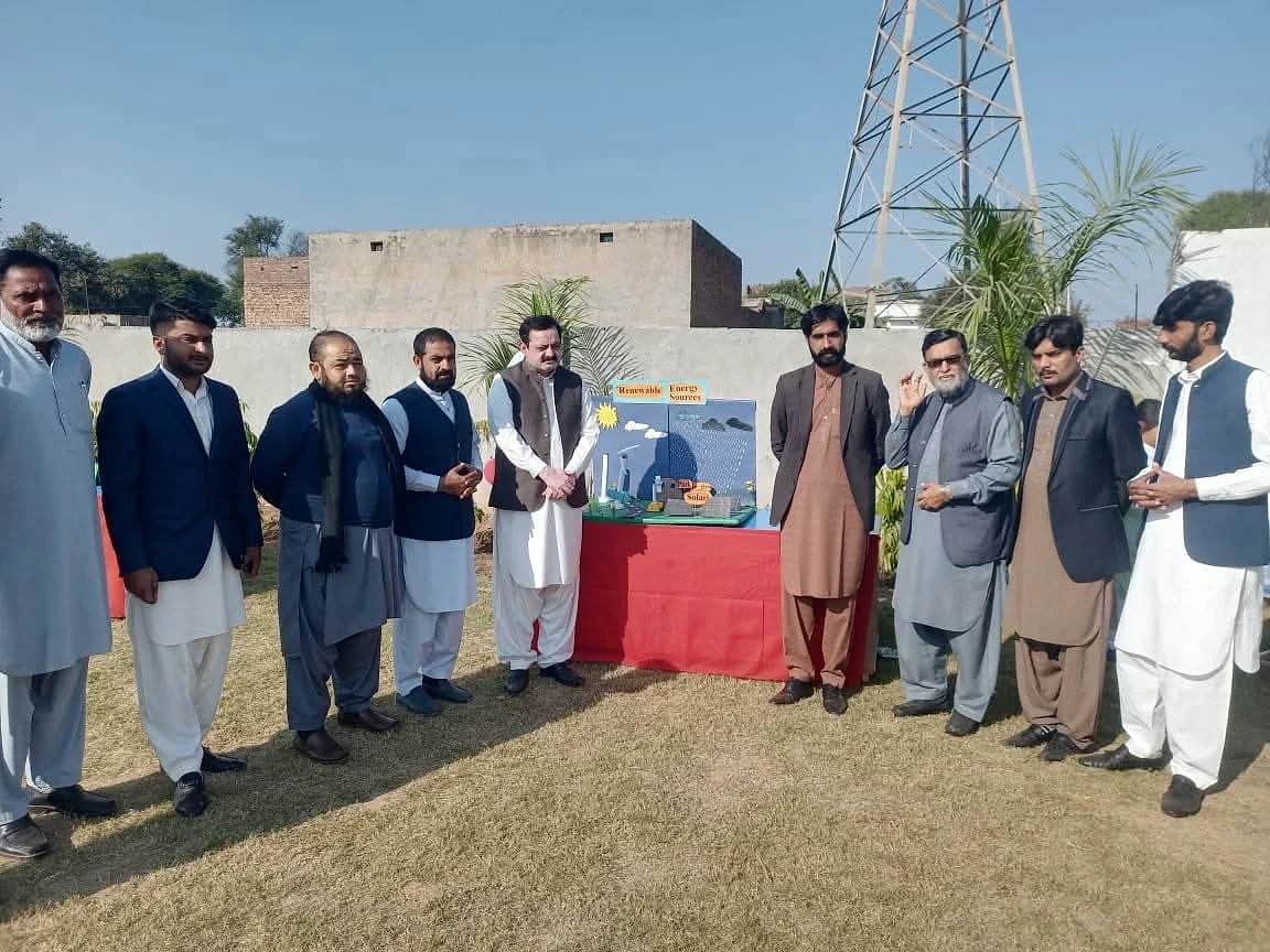 A group posing beside school project displays on a grassy outdoor area.